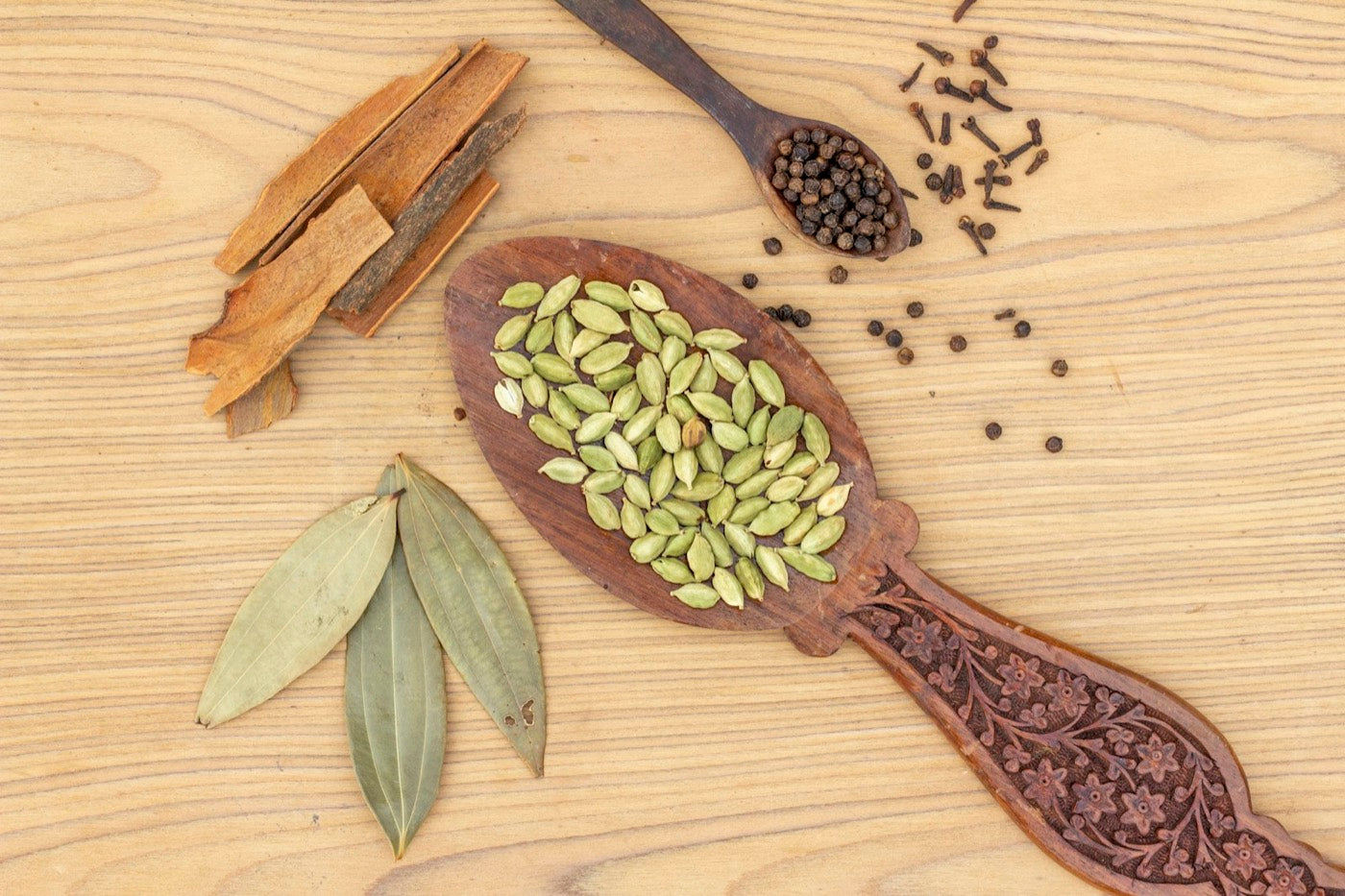 Cardamom pods and seeds on a wooden spoon