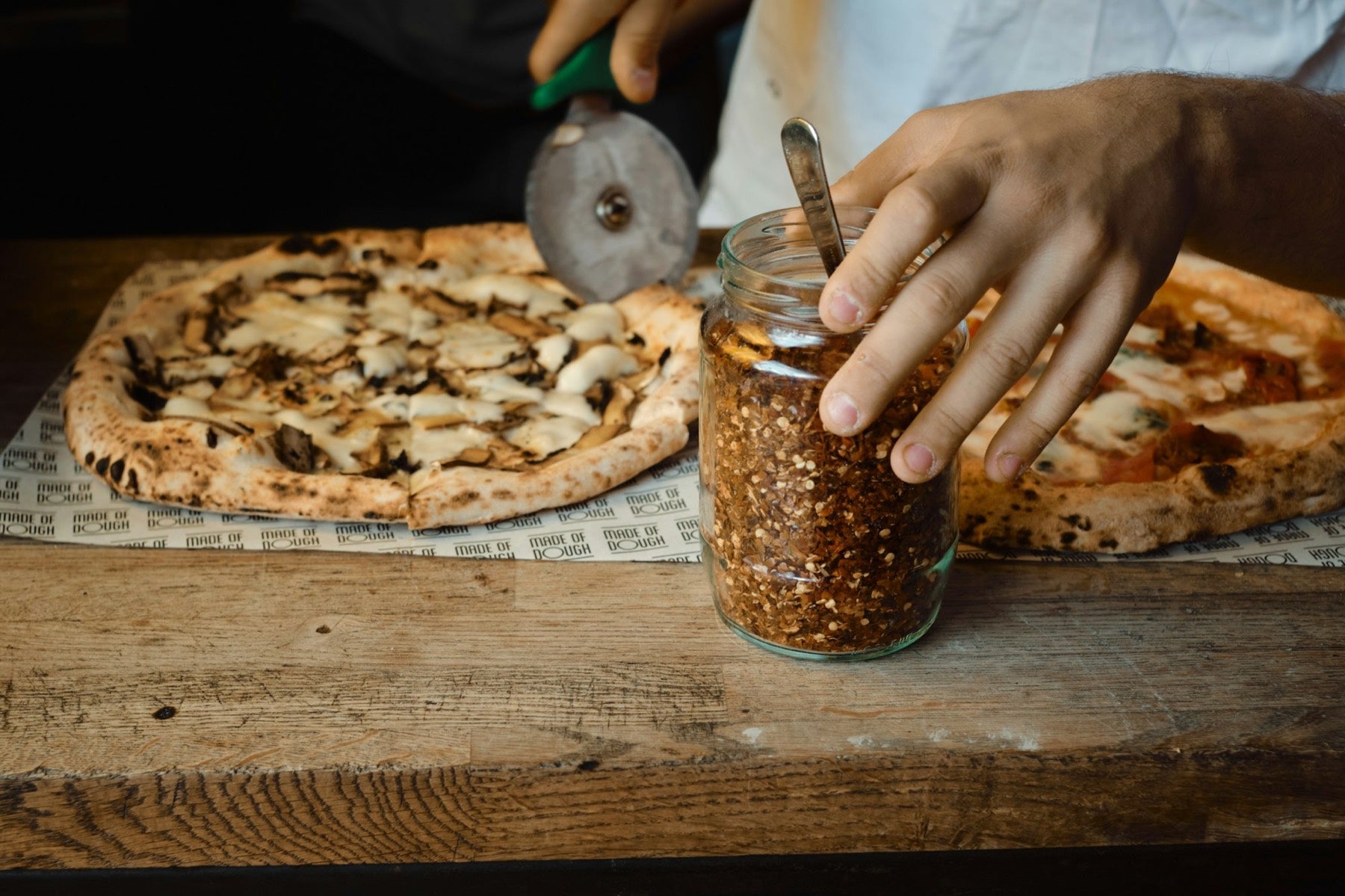 Pizza qu’on découpe, avec un bocal de flocons de piment à côté