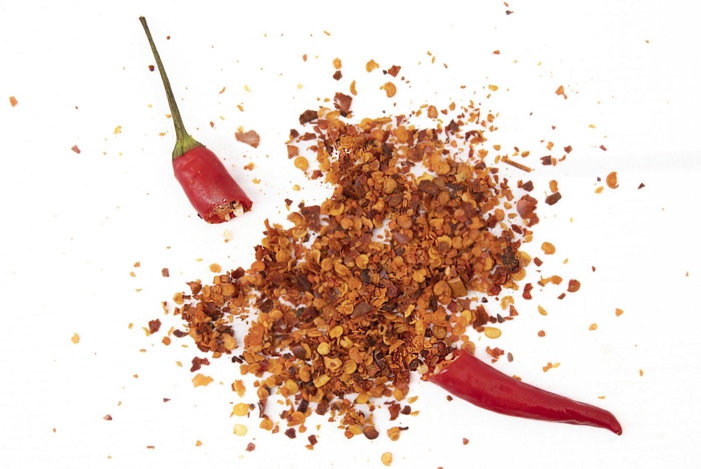 Flocons de chili et un piment entier séché sur une surface blanche